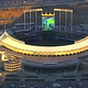 Ilustración para el artículo titulado La cámara de un helicóptero caza a un grupo jugando a Mario Kart en la pantalla gigante de un estadio de béisbol